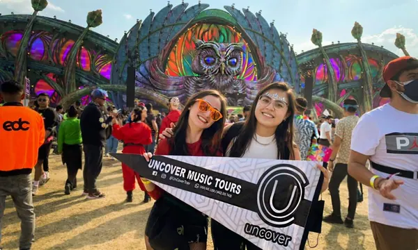 Dos viajeras de Uncover con la bandera del tour frente al escenario principal de EDC